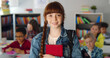 © TommyStockProject - Portrait of pretty redhead schoolgirl holding book and smiling at camera standing in classroom