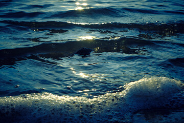 Wall Mural - Waves and foam on the beach during sunset.
