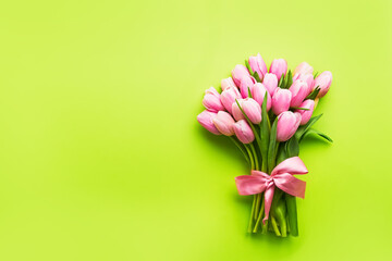 Pink tulips bouquet decorated with ribbon on a bright green background. Mothers Day, Valentines Day, birthday celebration concept.
