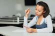 Portrait of teenage African-American girl in high school sitting at desk and chewing bubblegum while using smartphone in classroom, copy space