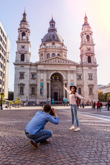 Young couple take pictures of each other while standing in front of St. Stephens Basilica in Budapest.