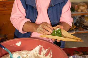 Indigenous woman preparing tamales with masa, stuffed with vegetables, covered by a corn leaf, traditional Mexican food.