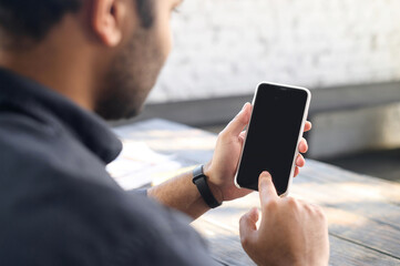 Back view mixed-race guy is using smartphone device with a blank screen, a man is scrolling and tapping touchscreen, using mobile app, mockup, copy space, advertising concept