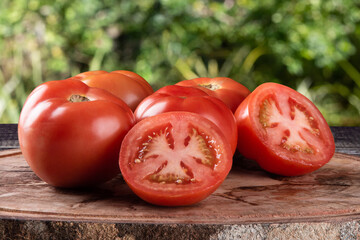 Ripe tomatoes cut on wood with blurred green background