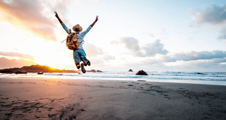 Wall Mural - Happy man with backpack jumping over the beach at sunset - Hiker enjoying freedom outdoor on sunshine - Success, travel and people concept
