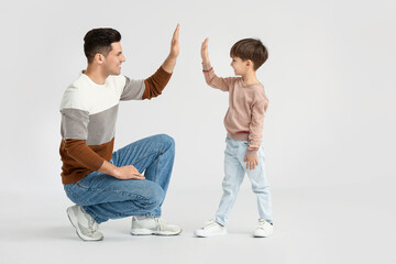 Wall Mural - Happy father and his little son giving each other high-five on light background