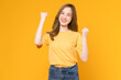 Cheerful beautiful Asian woman in a yellow t-shirt raises arms and fists clenched with shows strong powerful, celebrating victory expressing success.