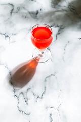 Wall Mural - A red berry cocktail or soda water in a glass, in direct hard light, long shadow, marble background, copy space