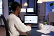 © DC Studio - Back view of african business woman analysing financial statistics working late at night. Focused employee doing overtime for job respecting deadline of project writing, searching.