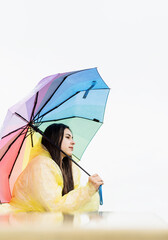 Wall Mural - Portrait of beautiful thoughtful woman standing outdoors holding a rainbow colored umbrella, looking away