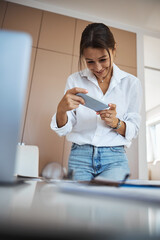 Wall Mural - Charming woman taking picture with smartphone in office