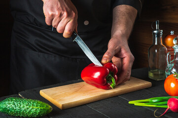 A professional chef is cutting red peppers for salad on a restaurant kitchen table. Vegetable diet or snack idea