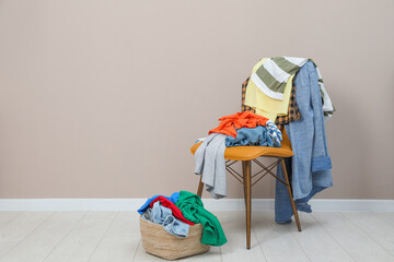 Sticker - Orange chair and wicker basket with different clothes near light grey wall, space for text