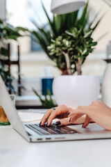 Woman typing on keyboard of a laptop at table in modern office