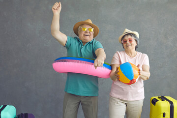 Studio portrait of two active elder tourists ready for tropical getaway travel summer vacation. Happy old people dancing and having fun with beach toys. Excited senior couple enjoying holiday shopping