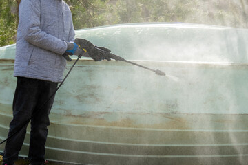 Close up of hand with gloves spraying compressed water to clean dirt of the boat surface outside. Sailboat maintenance.