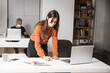 © Carles Iturbe/Wirestock - Young businesswoman standing in her home office writing notes - business concept