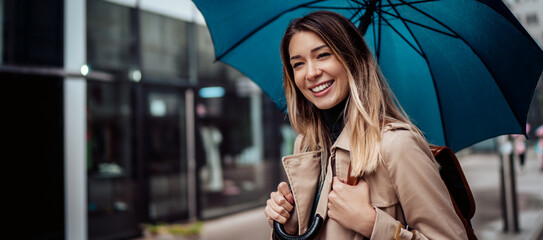 A beautiful smiling young woman walking through the city with an umbrella.