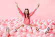 © GVS - Young happy woman with hands up sitting in pink balloons on pastel pink background