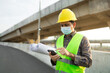© anut21ng Stock - asian man construction worker wear protective face masks and user smart phone against construction site background