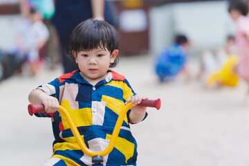 adorable 2-3 year old asian boy riding tricycle at playground. baby was sweating on his face due to 