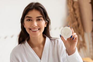 Wall Mural - Happy Young Lady Showing Cream Moisturizer Jar Posing In Bathroom