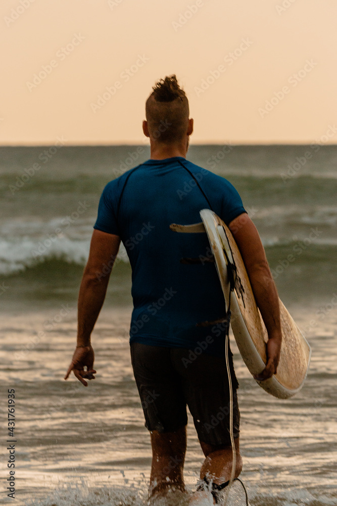 Surfer z deską surfingową na tle oceanu, mężczyzna uprawiający zdrowe sporty wodne. - obrazy, fototapety, plakaty 