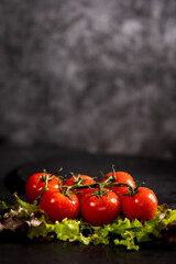 Roten Strauchtomaten liegt auf dem Salat auf dem schwarzen Tisch. Der Hintergrund ist fleckig Schwarz und grau. Gesunde Ernährung, Vegitaria, Vigan. Oben viel Platz zum Beschriften.