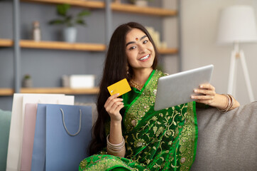 Wall Mural - Attractive Indian woman in ethnic sari dress using credit card and tablet computer for online shopping at home