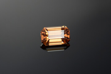 Wall Mural - Natural mined yellowish brown cognac color emerald cut flawless transparent zircon loose gemstone setting for making jewelry on dark gray gradient background. Reflection on black glass surface.