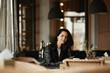 Portrait of a young female model with dark hair wearing leather jacket sitting at the table in a cafe