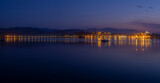 Fototapeta Pomosty - Panorámica nocturna del puente de San Vicente de la Barquera iluminado , con los reflejos de las luces de colores en el mar, y las barcas meciéndose en el agua, en Santander, España, verano de 2020.