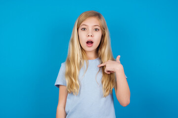 Wall Mural - beautiful Caucasian little girl wearing white T-shirt over blue background being in stupor shocked, has astonished expression pointing at oneself with finger saying: Who me?