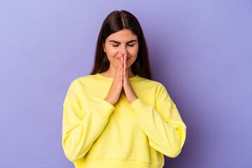 Young caucasian woman isolated on purple background holding hands in pray near mouth, feels confident.