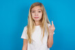 beautiful Caucasian little girl wearing white T-shirt over blue background shows middle finger bad sign asks not to bother. Provocation and rude attitude.