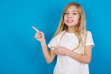 Wall Mural - beautiful Caucasian little girl wearing white T-shirt over blue background points at copy space indicates for advertising gives right direction