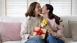 © ChayTee - Attractive beautiful asian middle age mum sit with grown up daughter give gift box and flower in family moment celebrate mother day. Overjoy bonding cheerful kid embrace relationship with retired mom.