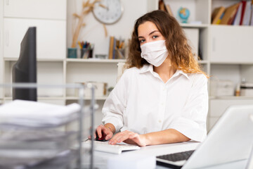 Wall Mural - Young female employee works in modern office with social distance and personal protective equipment