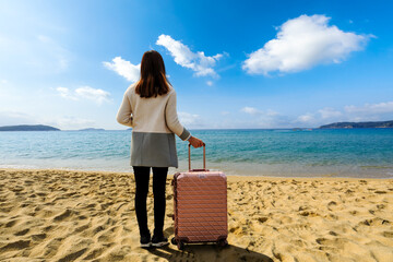 Young woman with large suitcase on tropical beach.