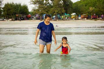 mother and daughter walking on sea and playing in the waves at sea in Thailand,cute baby have fun on vacation.