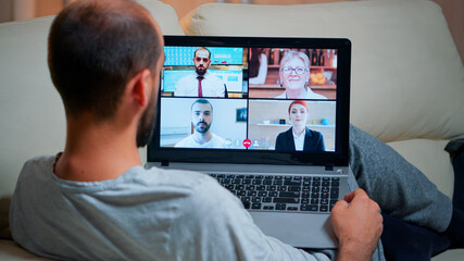 Poster - Focused adult using laptop computer during videocall conference talking about social business connection while sitting on couch. Relaxed man working at online communication project overtime in kitchen