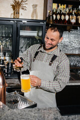 Wall Mural - Close-up of a bearded bartender filling a mug of lager beer. The bar counter in the pub.