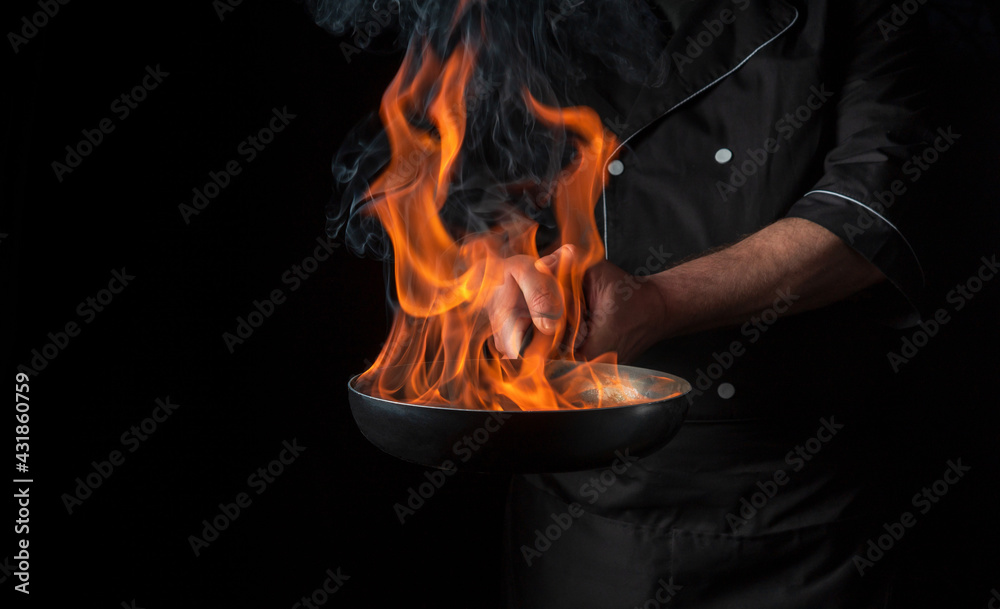 Chef cooking food in pan with fire flame on black background ...