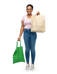 Sticker - sustainability and people concept - happy smiling young african american woman comparing green reusable canvas bag for food shopping with paper bag over white background