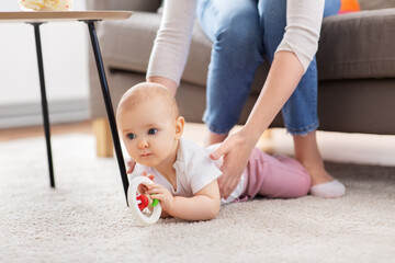 Wall Mural - family, motherhood and people concept - mother and little baby daughter playing with rattle toy on floor at home