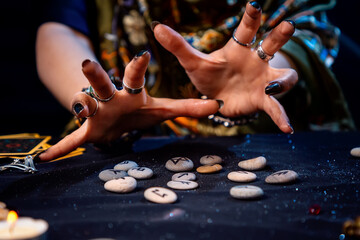 Wall Mural - Female hands of a fortune teller reads scandinavian runes. The concept of divination, astrology and predicting the future