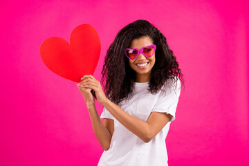 Wall Mural - Photo of romantic curly millennial lady hold heart look empty space wear white t-shirt isolated on pink color background