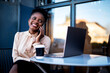 © JustLife - Businesswoman talking to the phone. African woman with laptop in coffee shop..