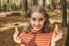 Portrait Of A Funny Little Girl In Nature. She Holds Edible Mushrooms In Her Hands. Outdoor Fun And Vacation Concept.