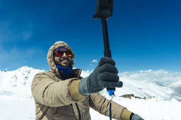 Young and handsome male travel blogger recording a video for vlog with his Go Pro action camera, making vlog for youtube in the snow mountains.